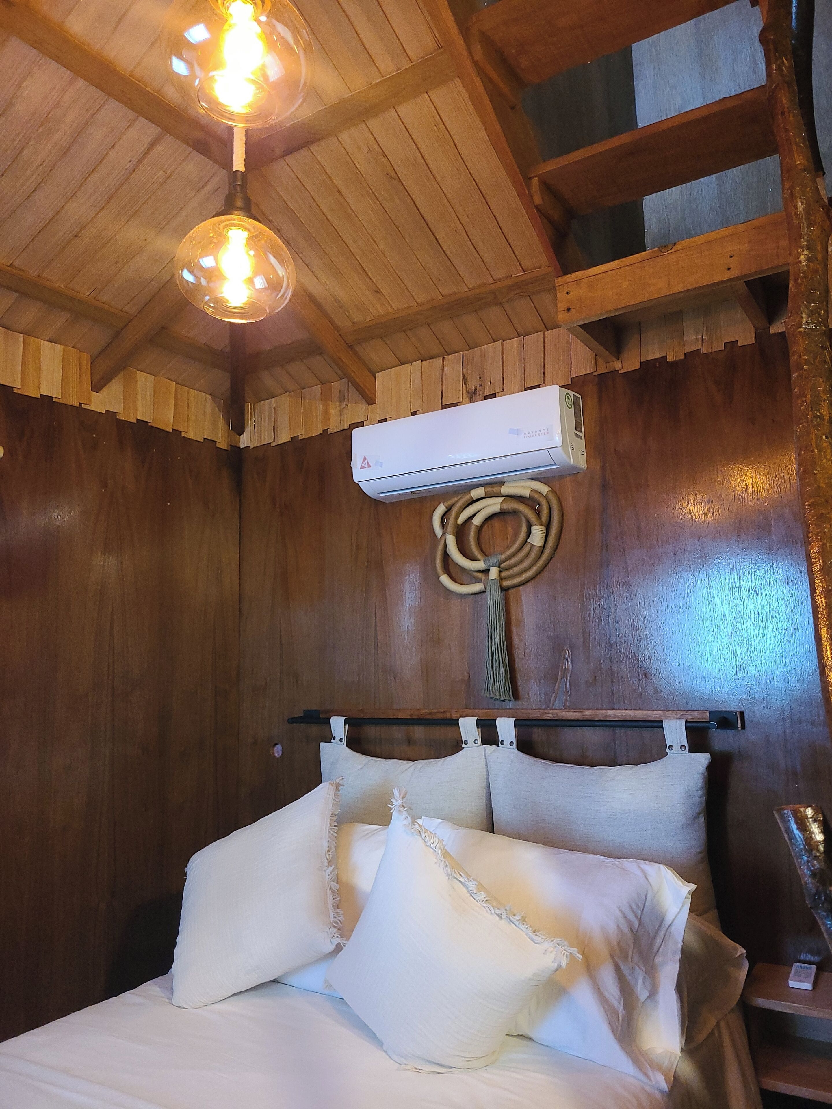 A wooden room with a bed, a hanging light fixture, and an air conditioning unit.