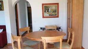 A dining area with a wooden table and chairs, a painting on the wall, and a wooden cabinet.