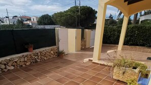 A patio with tiled flooring, a stone wall, and potted plants.