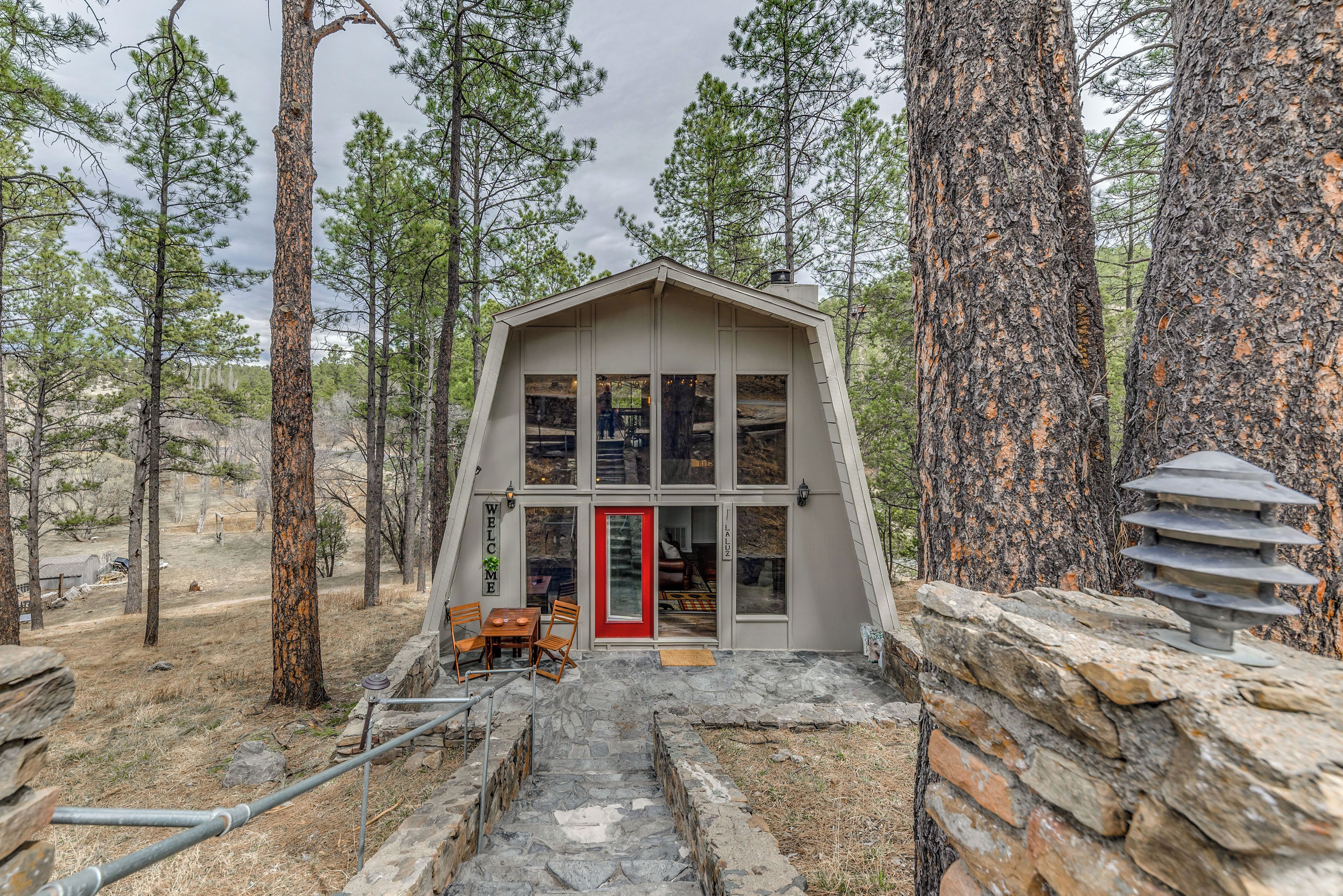 A modern cabin with a red door, stone steps, and a stone wall.