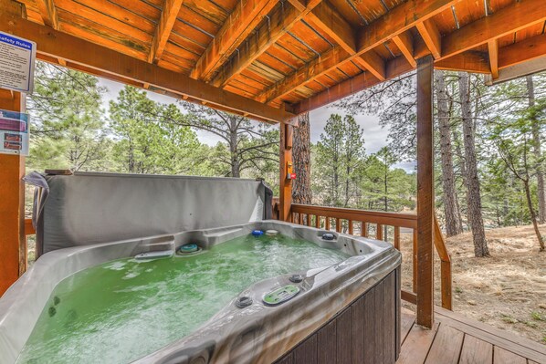 A hot tub under a wooden deck with a view of trees. - Cozy Ruidoso Cabin Rental w/ Private Hot Tub! (Ruidoso)