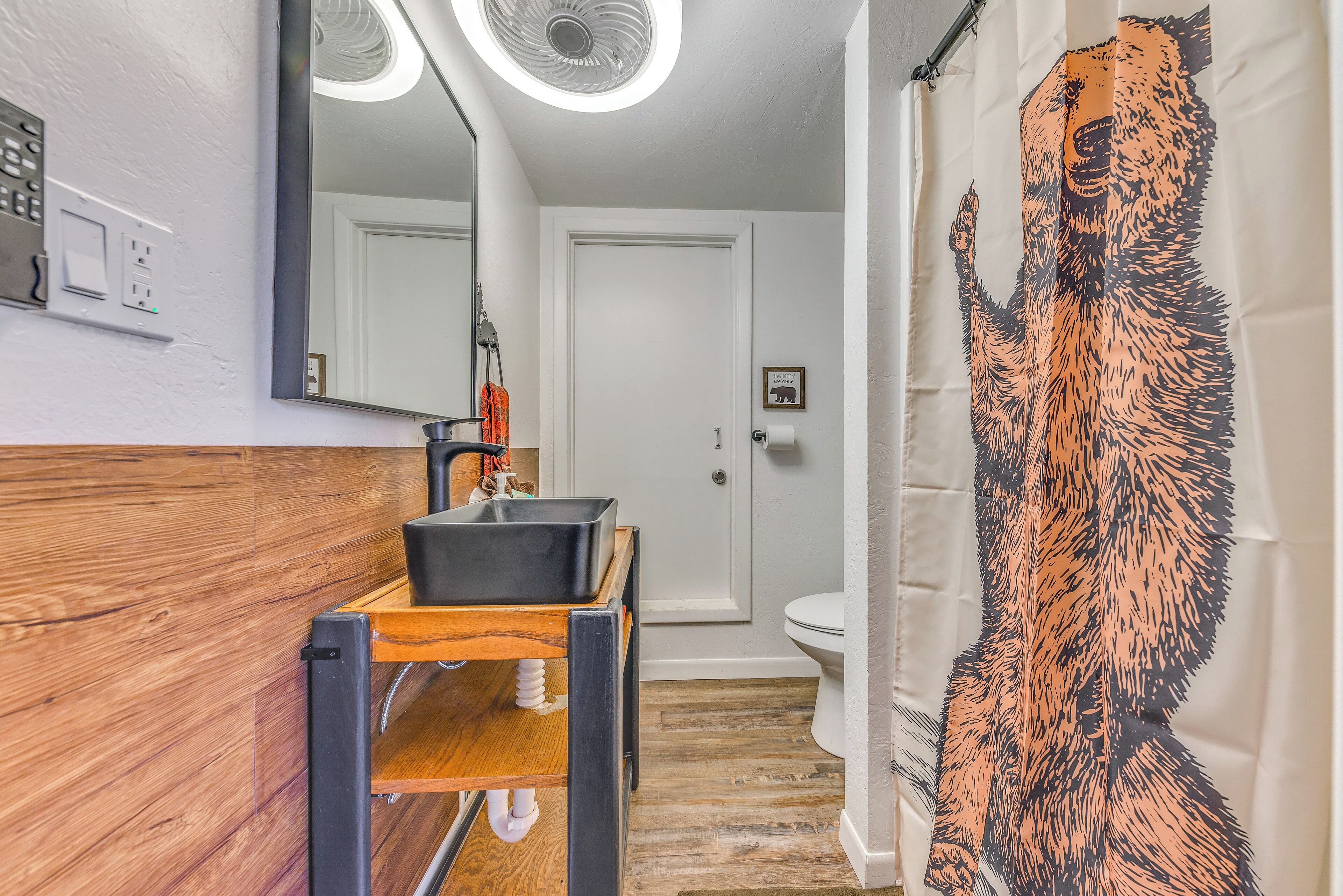 Un baño con tocador de madera, lavamanos negro, espejo y cortina de ducha con diseño de perro.