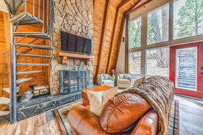A cozy cabin interior with a stone fireplace, a wooden staircase, and a leather couch. - Cozy Ruidoso Cabin Rental w/ Private Hot Tub! (Ruidoso)