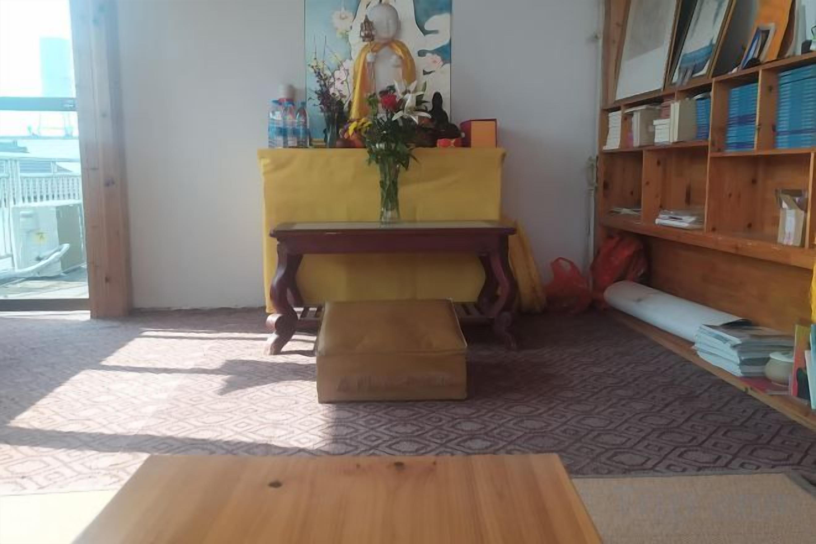 Una habitación con una mesa de madera, un altar amarillo y una estantería.