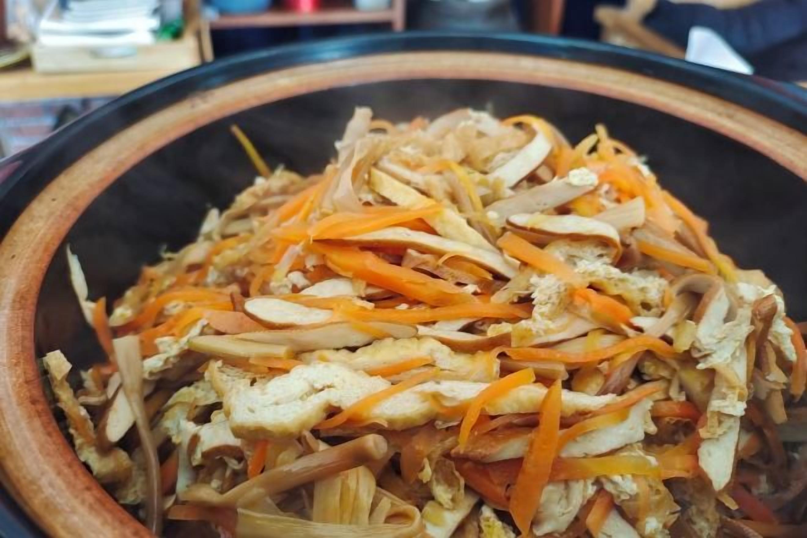 A large wooden bowl filled with shredded chicken and carrots.