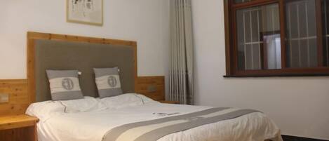 Una camera da letto con una testiera in legno, un letto con biancheria bianca, un comodino, una finestra con persiane e un quadro incorniciato appeso al muro.