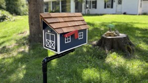 Una casa modelo con techo marrón y puerta roja, montada sobre un tubo negro.