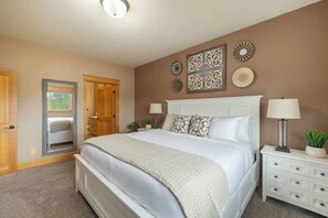 Een slaapkamer met een groot bed, nachtkastje met lamp, een dressoir en decoratieve wandkunst.