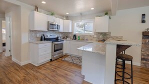 A modern kitchen with white cabinetry, stainless steel appliances, a granite countertop, and a wooden floor. - The Silver Mountain Chalet- Private Hot Tub! (Kellogg)