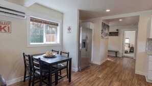 A modern kitchen with a stainless steel refrigerator, a dining table with chairs, and a window with blinds. - The Silver Mountain Chalet- Private Hot Tub! (Kellogg)