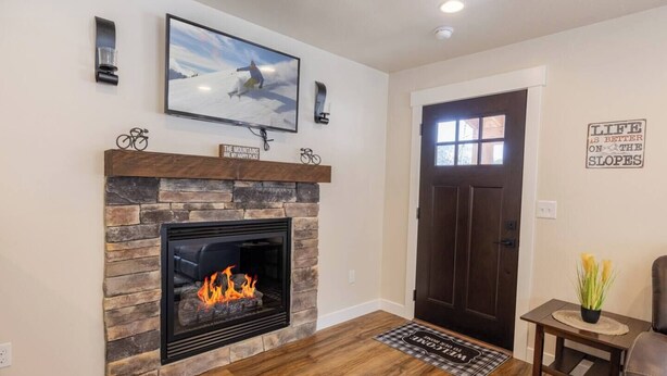 A living room with a stone fireplace, a television mounted above it, and a door with a window. - The Silver Mountain Chalet- Private Hot Tub! (Kellogg)