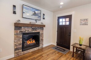 A living room with a stone fireplace, a television mounted above it, and a door with a window. - The Silver Mountain Chalet- Private Hot Tub! (Kellogg)