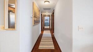 Un couloir doté d’un plancher en bois, de murs blancs et d’un luminaire au plafond.