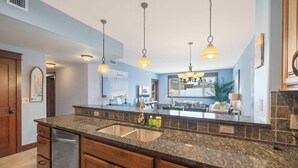 Une cuisine moderne dotée de plans de travail en granit, d’un évier en acier inoxydable, de meubles en bois et d’un éclairage suspendu.