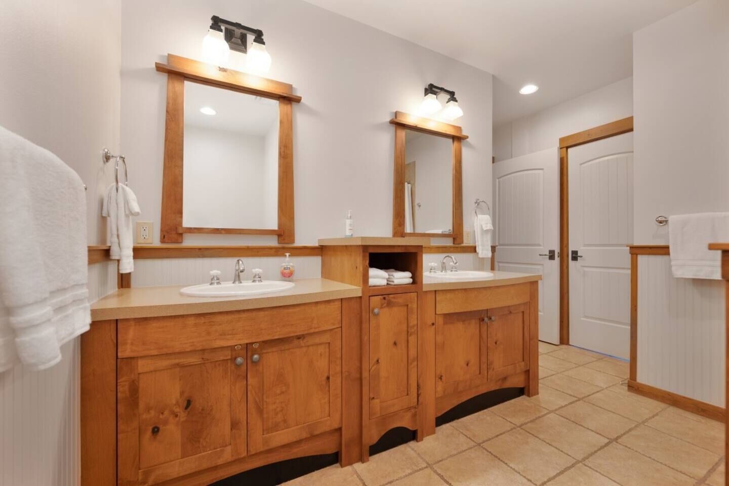 A modern bathroom with two sinks, wooden cabinets, and large mirrors.
