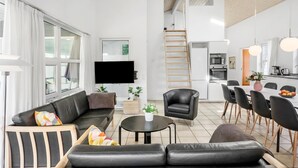 Ein modernes Wohnzimmer mit einer Couch, einem Couchtisch und einem Fernseher. Es gibt eine Küchenzeile mit einem Esstisch und Stühlen.