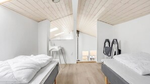 Ein Zimmer mit zwei Betten, einer hohen Decke mit Holzbalken, einem Oberlicht und Blick ins Freie.