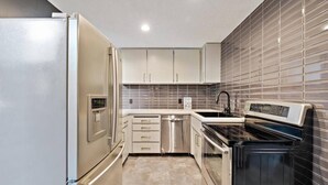 A compact kitchen with a refrigerator, dishwasher, stove, and a tiled backsplash. - Broomsticks, Harry Potter themed BNB, Hot Tub! (Coeur d'Alene)