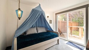 A bedroom with a canopy bed, a hanging light fixture, and a view of the backyard through a sliding glass door. - Broomsticks, Harry Potter themed BNB, Hot Tub! (Coeur d'Alene)