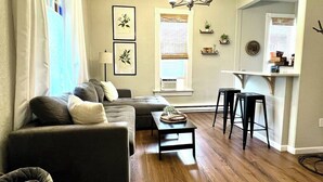 A living room with a sofa, a coffee table, and a kitchen area with stools. - The Flat on 5th-walk to dt! (Coeur d'Alene)