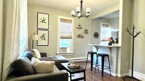 A living room with a sofa, coffee table, and a dining area with a table and chairs. - The Flat on 5th-walk to dt! (Coeur d'Alene)