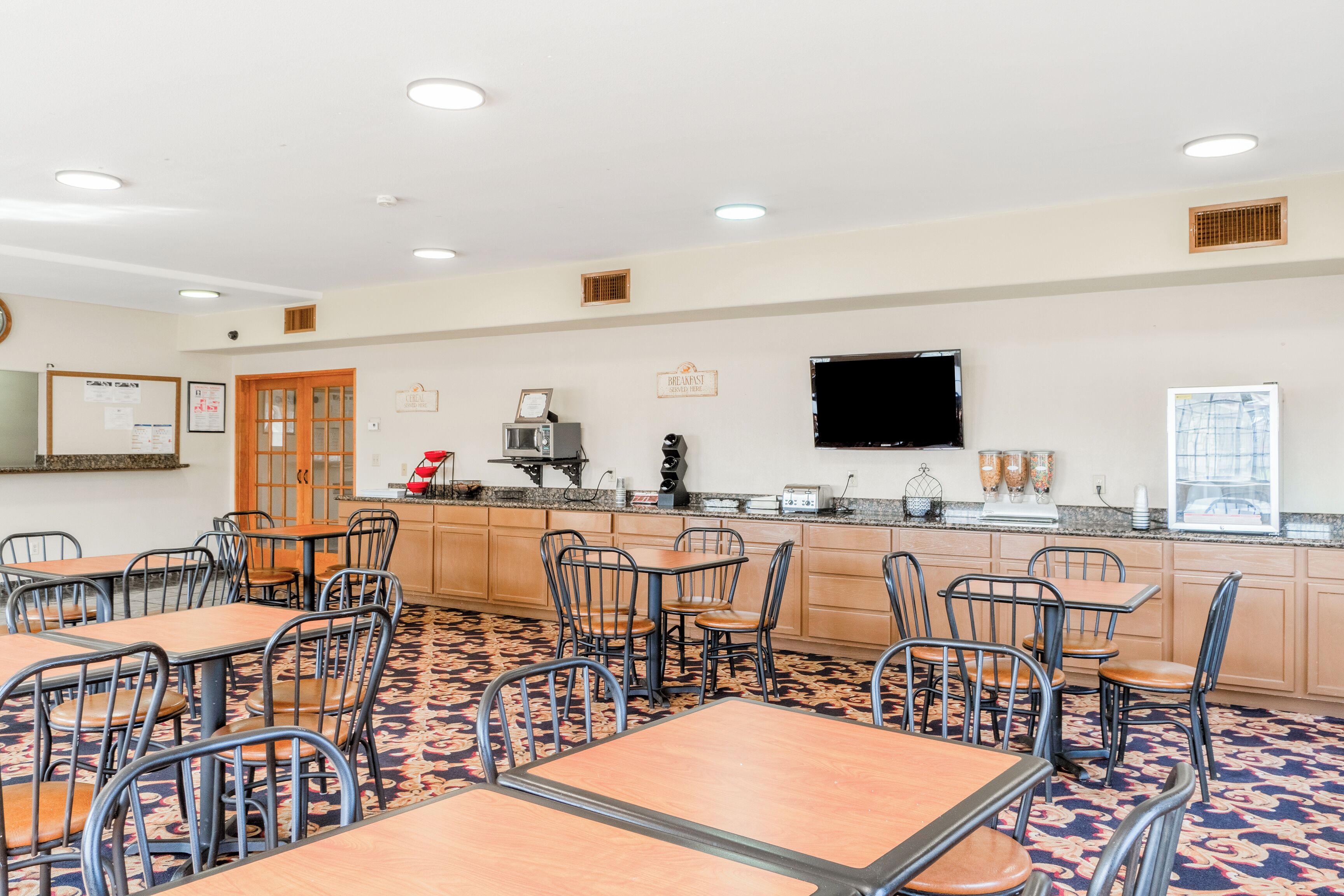 A dining area with tables and chairs, a kitchen counter, and a television mounted on the wall.