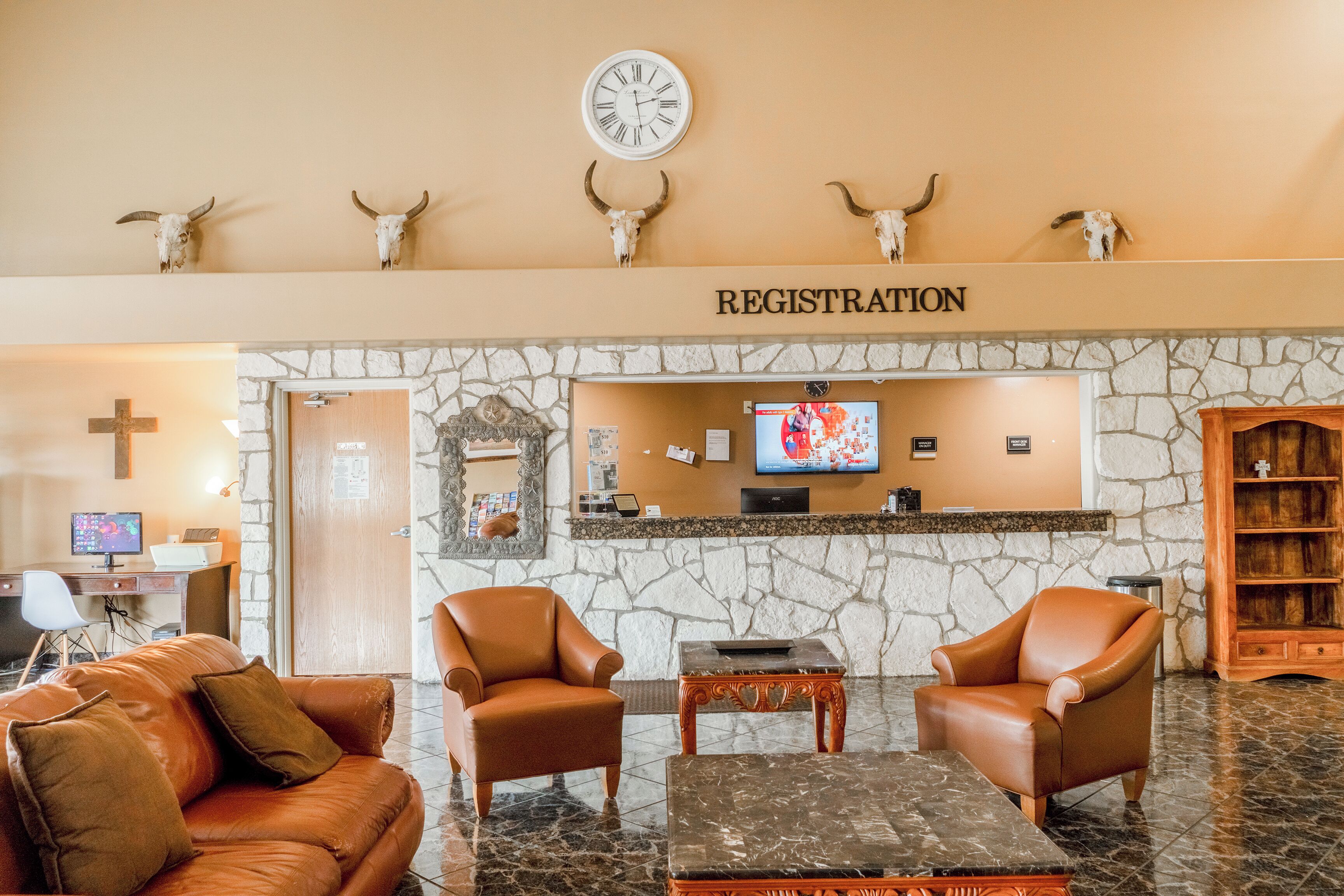 A lobby with a registration desk, leather chairs, a stone wall, and a television.