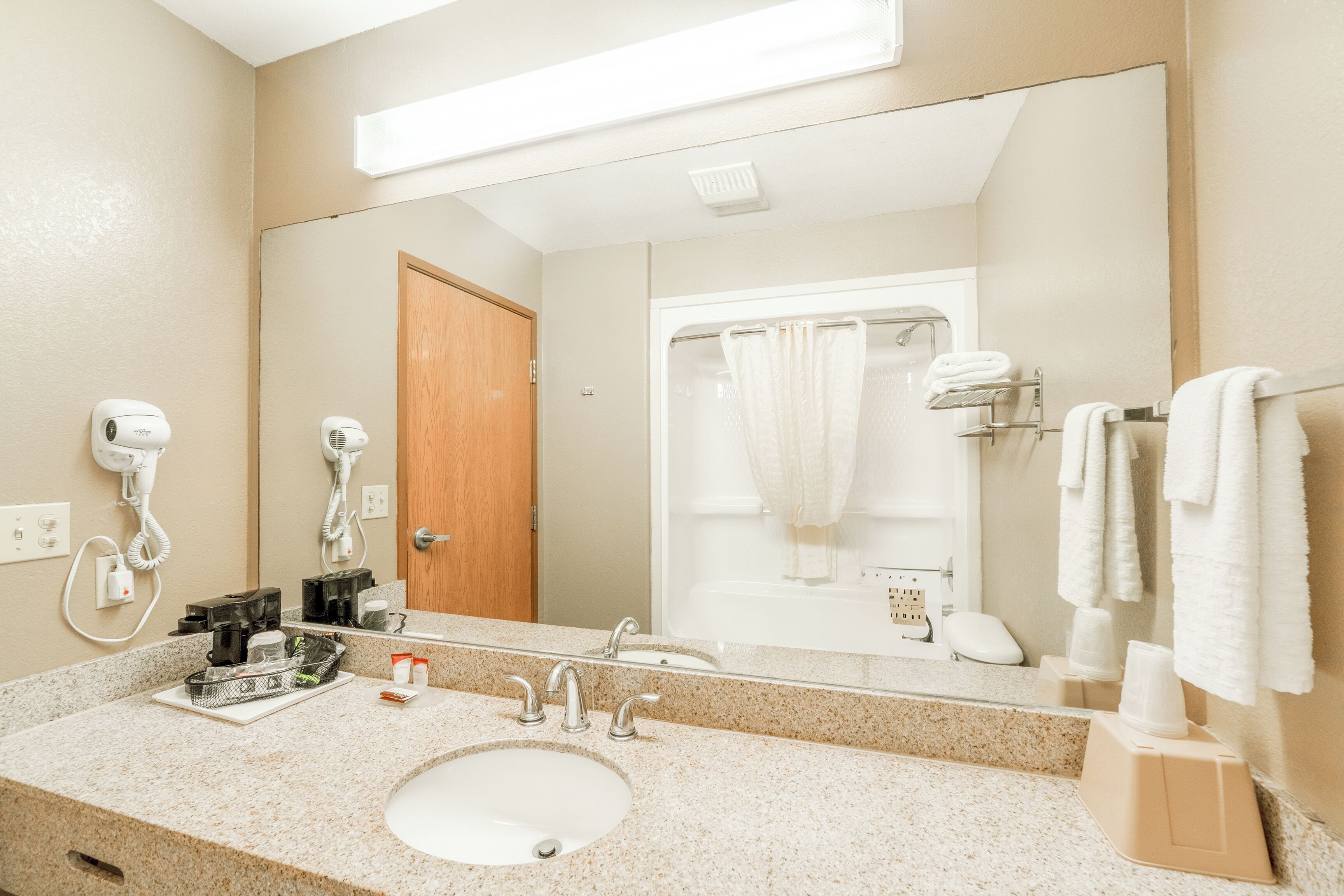 Un baño de hotel con lavamanos, espejo, secador de pelo y toallero.