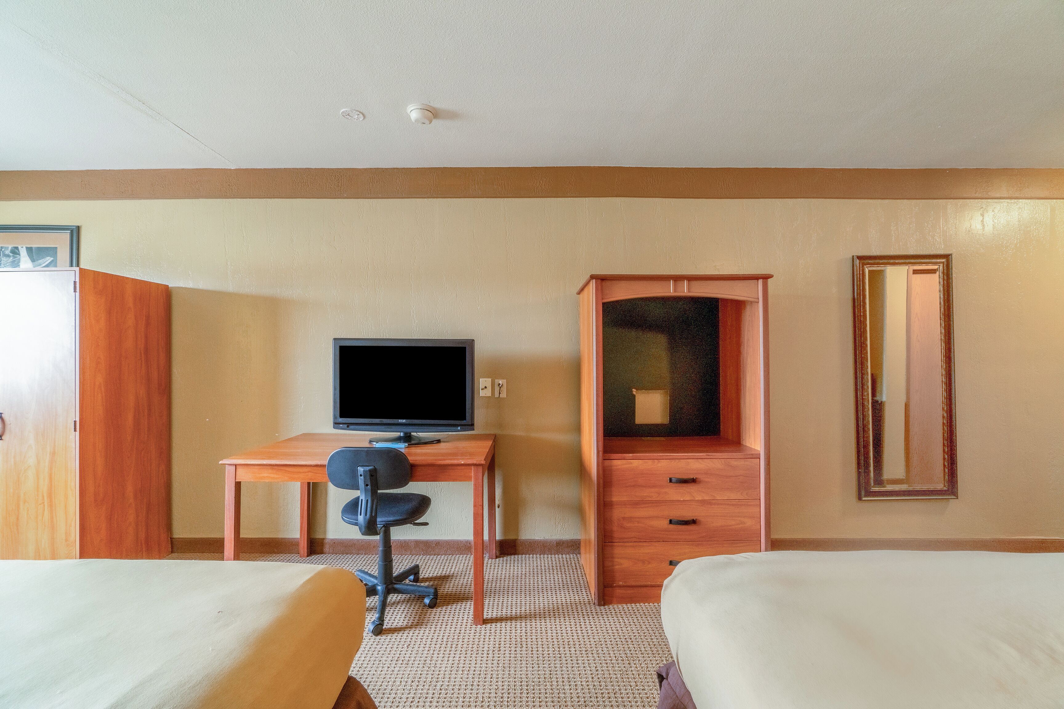 Habitación de hotel con dos camas, un escritorio con computadora, televisor, armario y espejo.