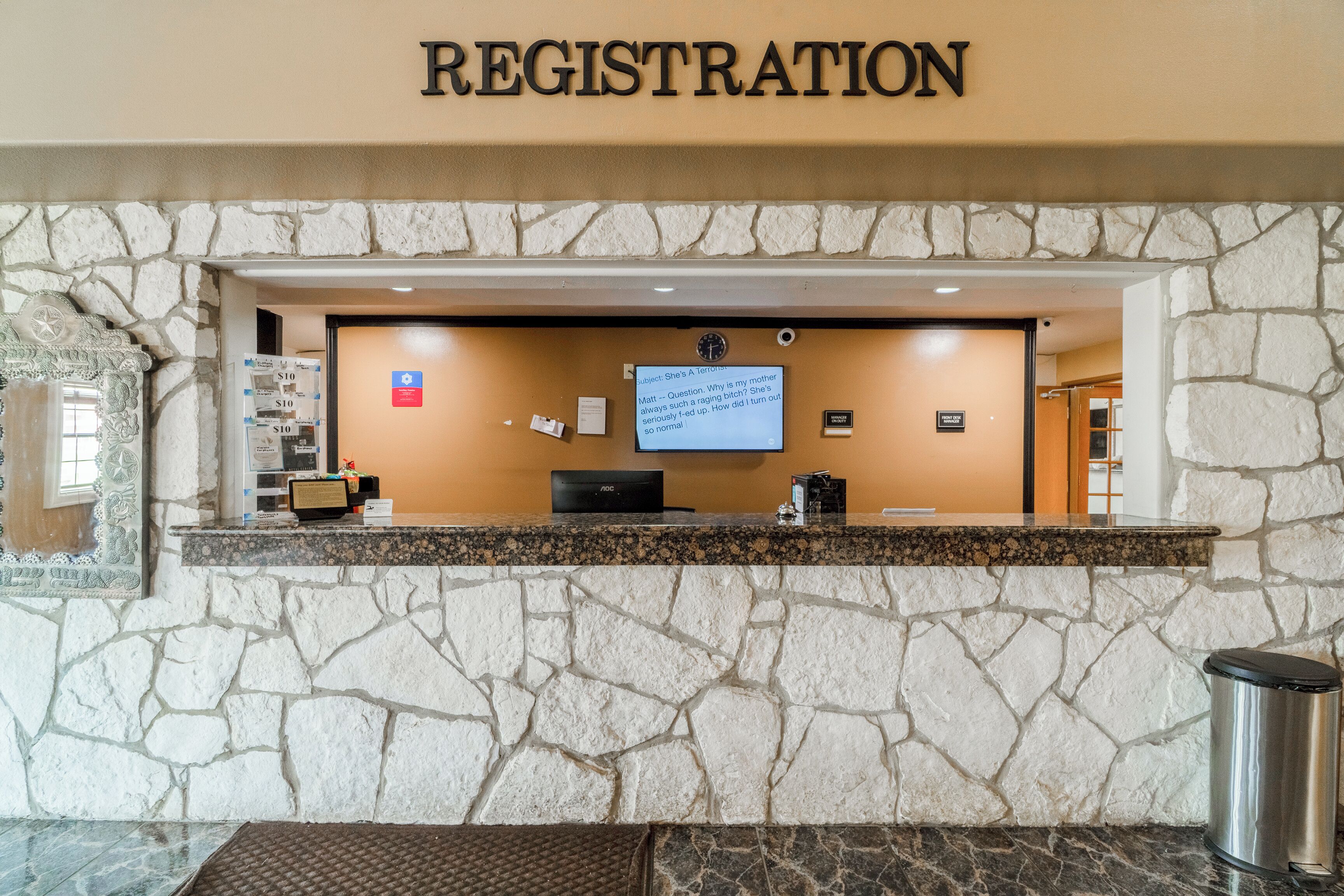 A registration desk with a stone wall backdrop, a computer, and a trash can.