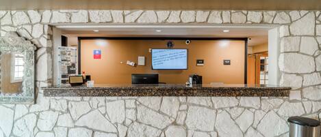 A registration desk with a stone wall backdrop, a computer, and a trash can.