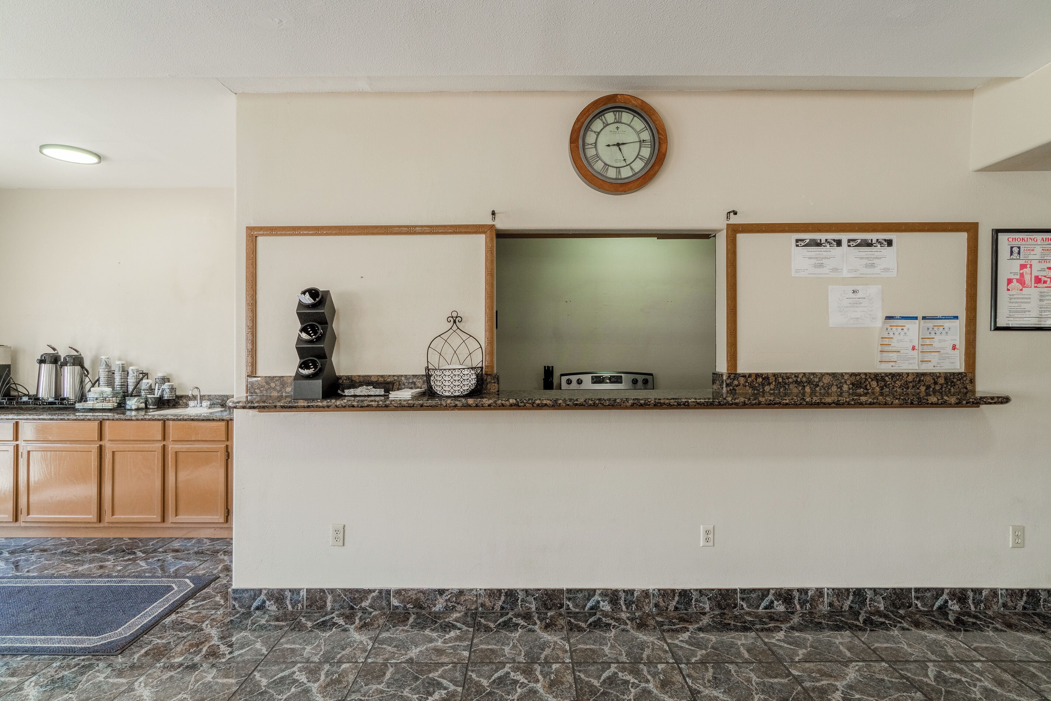 A reception area with a clock, bulletin board, and kitchen counter with appliances.