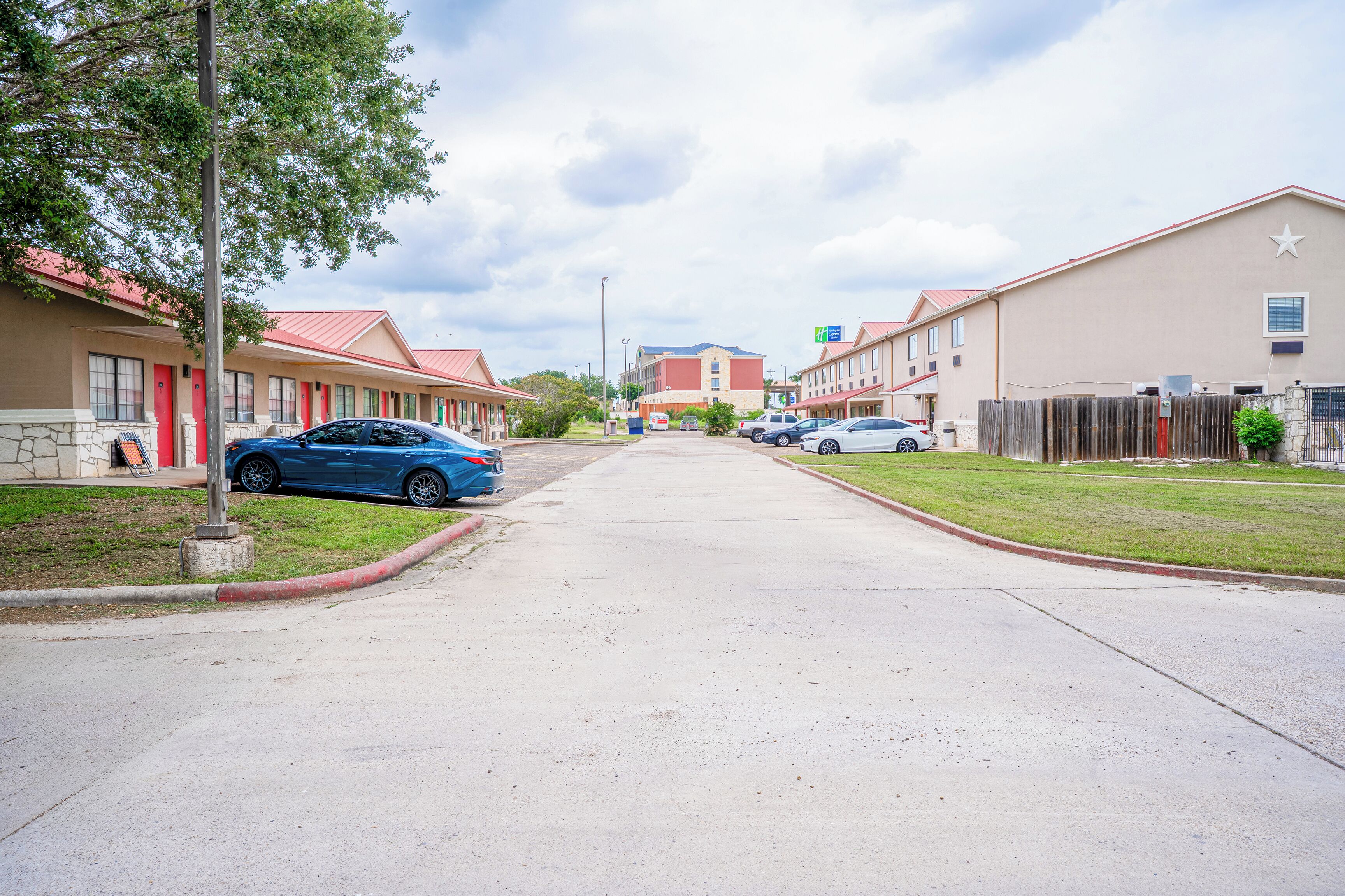 A street view of a motel with a row of single-story buildings, each with a red roof and beige walls.