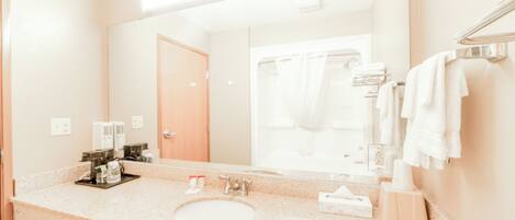 A hotel bathroom with a sink, mirror, towel rack, and shower area.