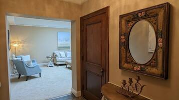 A hallway with a chandelier, a wooden door, a mirror with floral frame, and a seating area with a sofa and armchairs.