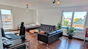 Een moderne woonkamer met een bank, een bureau met een laptop, een salontafel en een plant.