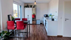 Een moderne keuken met witte kastjes, een eethoek met rode stoelen en een kleine koelkast.