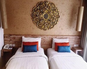 A hotel room with two beds, a wooden headboard, a decorative wall piece, and a hanging light fixture.
