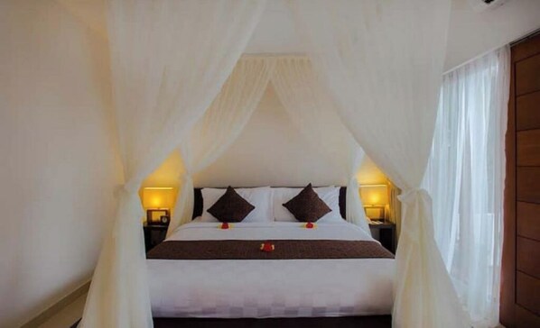 A bed with a canopy, two bedside tables with lamps, and a window with curtains.
