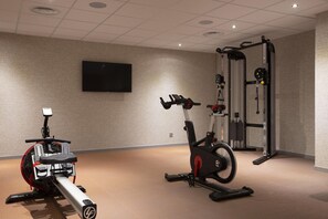 Une salle de sport équipée de machines de cardio, d’un téléviseur fixé au mur et d’un support pour les exercices de squat.