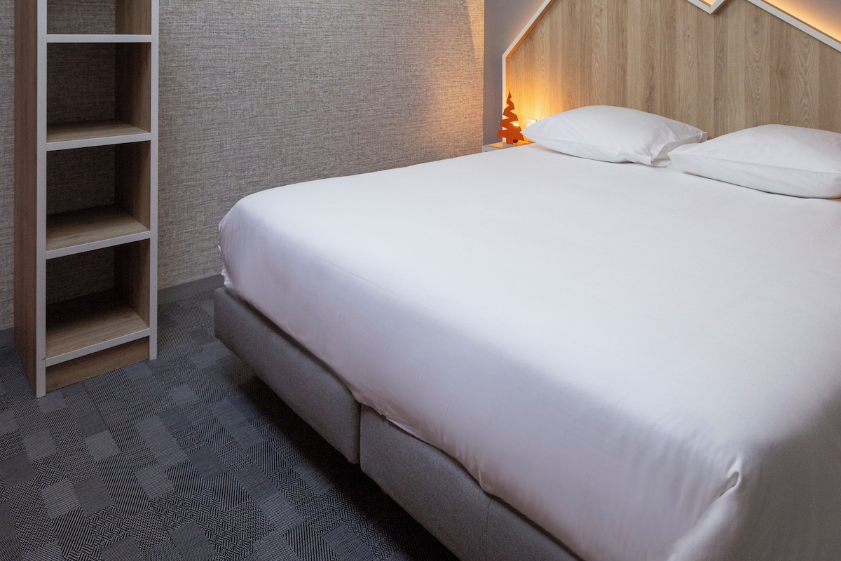 Un dormitorio moderno con tragaluz, estantería empotrada, cabecero de madera y mesita de noche con lámpara.