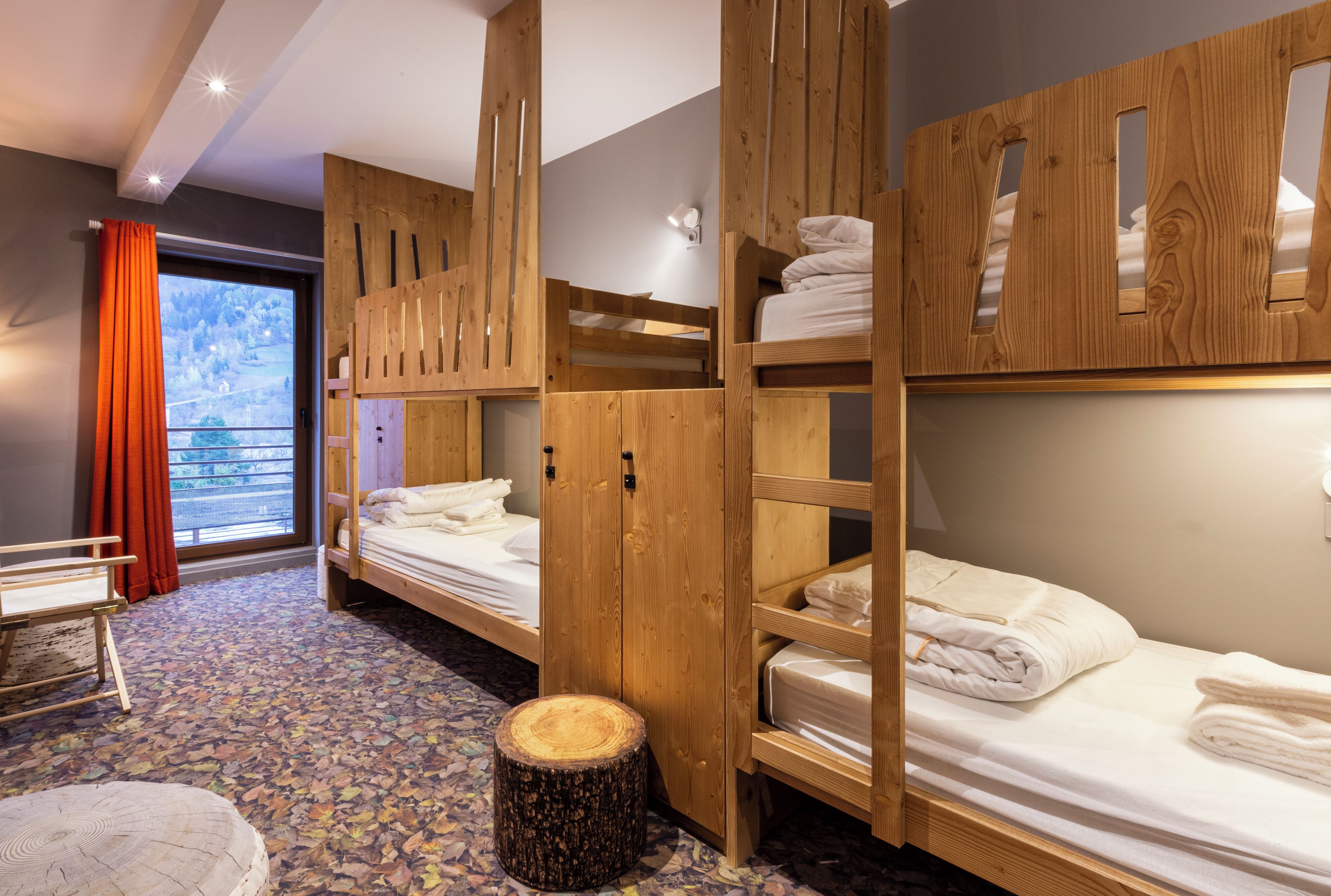Ein Zimmer mit Etagenbetten, Holzschränken, einem runden Hocker und einem Fenster mit Vorhängen.