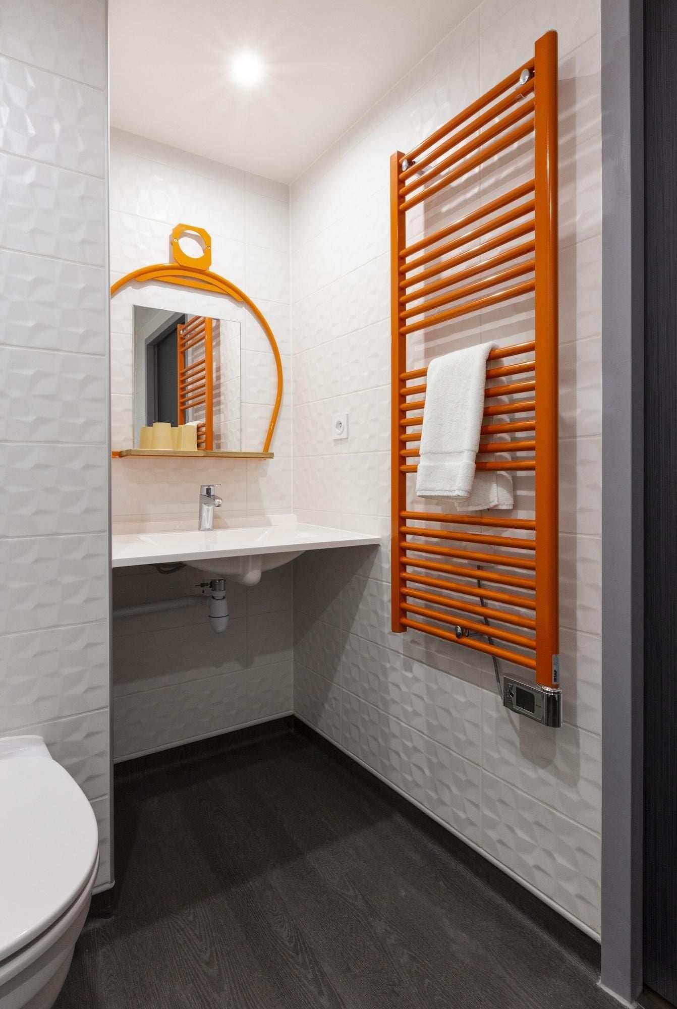 A modern bathroom with a white tiled wall, a wooden towel rack, a white sink, and a toilet.