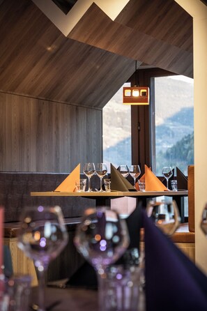 A restaurant with a wooden interior, a mountain view, and a table set with wine glasses and napkins. - Base Camp Lodge (Bourg-Saint-Maurice)