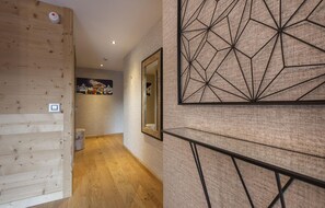 A hallway with wooden paneling, a geometric wall art piece, and a framed picture on the wall. - Base Camp Lodge (Bourg-Saint-Maurice)