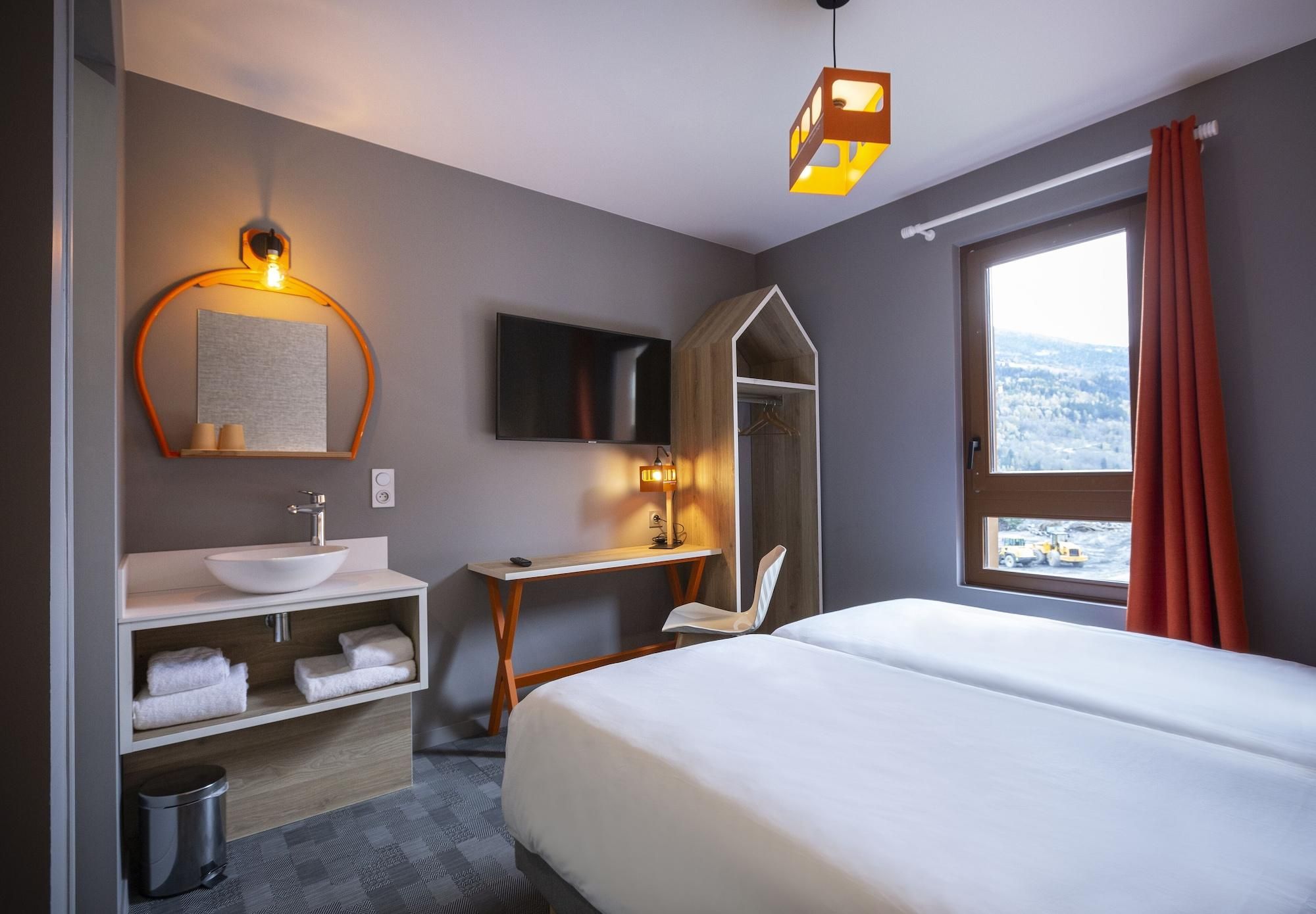 A hotel room with a bed, a TV, a desk, a mirror, a sink, and a window with a view.
