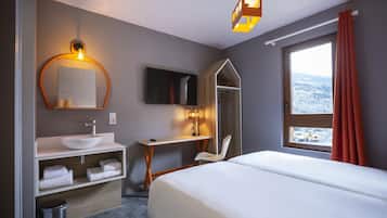 A hotel room with a bed, a TV, a desk, a mirror, a sink, and a window with a view.