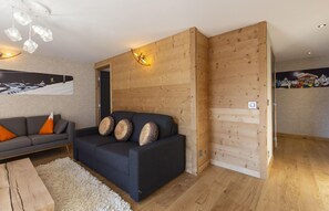 Een moderne woonkamer met een donkere bank, houten wandpanelen en een lichte houten vloer.