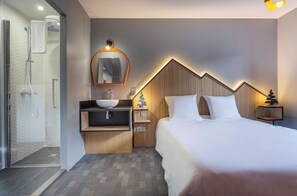 Une chambre d’hôtel avec un lit, une salle de bain avec une douche, un lavabo et un miroir.