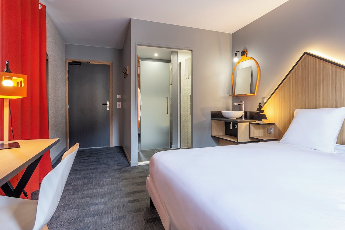 Hotelkamer met een bed, een bureau, een stoel, een bureaulamp, een nachtkastje, een spiegel en een douche.